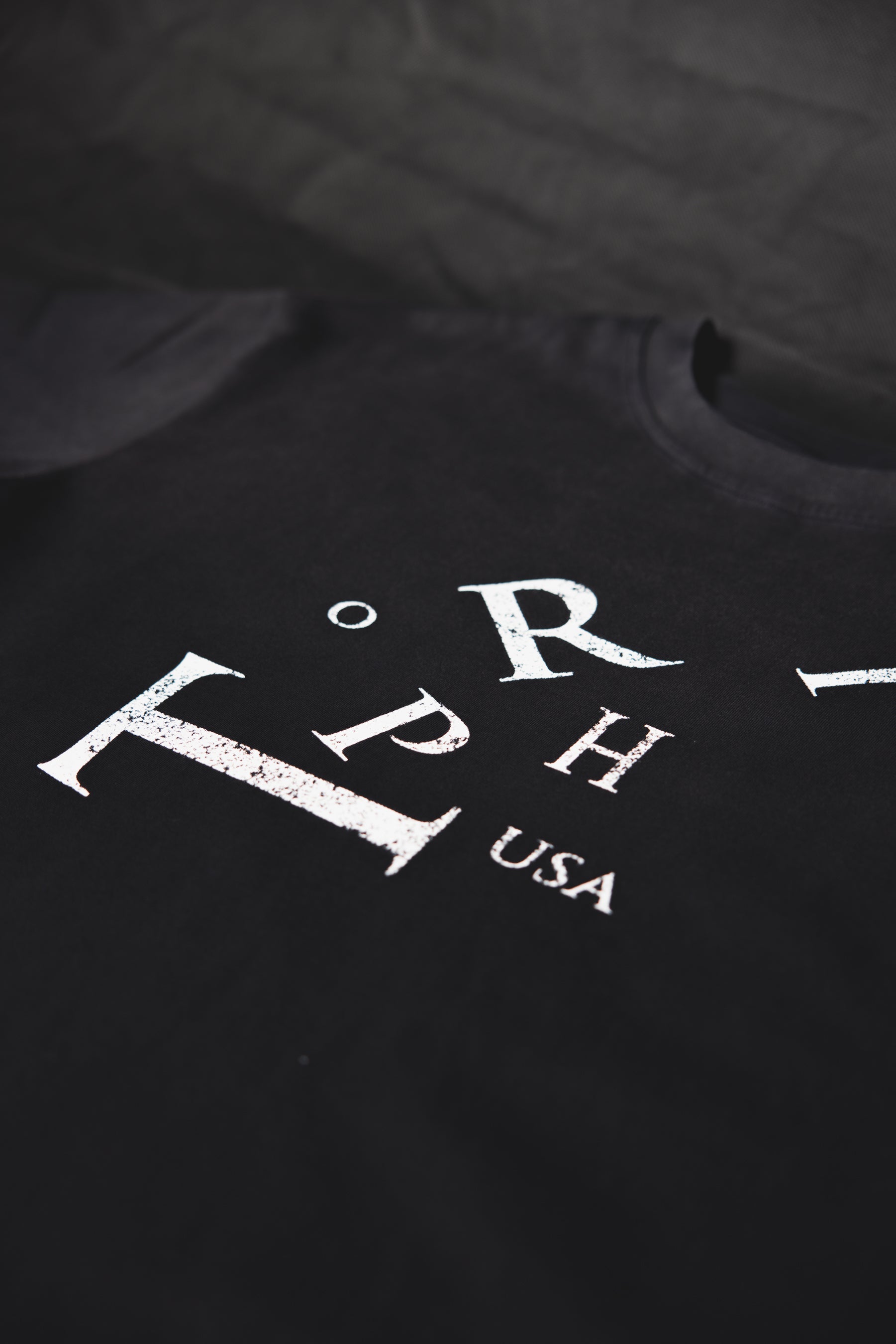 A close-up of a black t-shirt featuring a distressed white graphic print with the letters 'ORPH' and 'USA' on the chest.