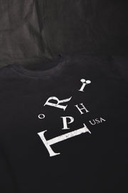 A black crewneck t-shirt featuring a distressed white graphic print of the letters 'RIP' and 'USA' on the front, laid flat against a dark fabric background.
